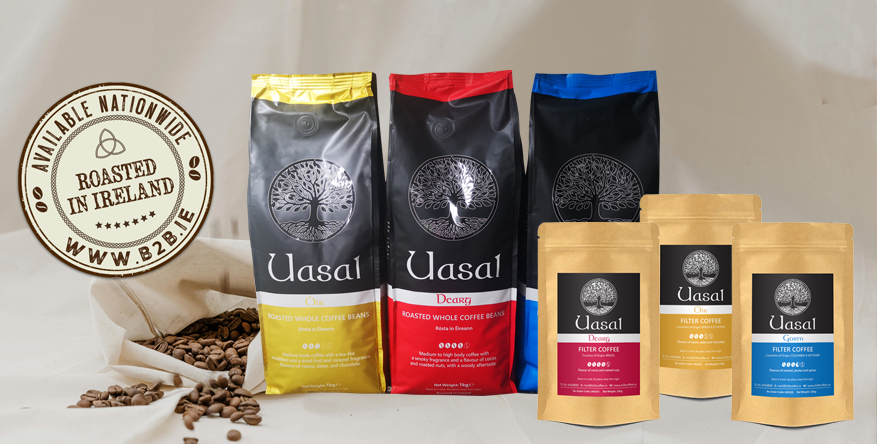 A wide product shot of the Uasal coffee collection, including 1kg whole bean bags and 250g filter pouches in gold, red, and blue, featuring a prominent "Available Nationwide - Roasted in Ireland" vintage-style seal.