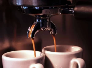 A close-up view of an espresso machine pouring fresh, dark coffee simultaneously into two white ceramic cups.