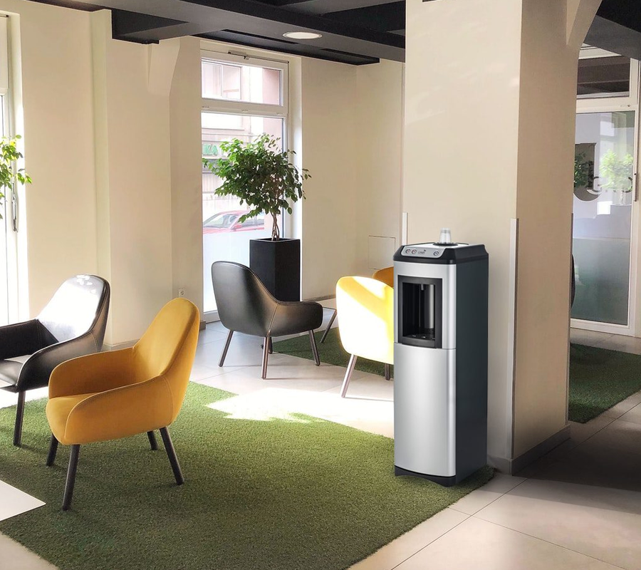 A sleek, Oasis KaliX Water Cooler situated in a modern office lobby with yellow and grey armchairs and green rugs.