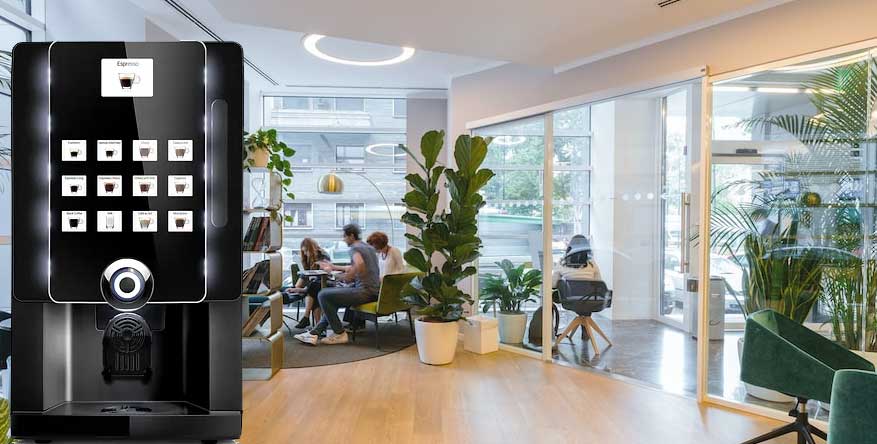A professional, black touchscreen coffee machine stands in the foreground, while a brightly lit, modern office lounge with people working and large plants is visible in the background.