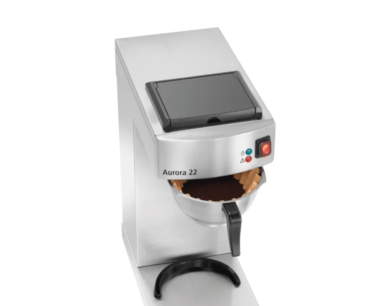 An overhead view of the Aurora 22 stainless steel coffee brewer with the filter basket pulled forward, filled with a pleated paper filter and fresh dark coffee grounds.