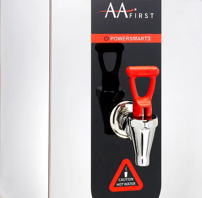 A close-up shot of the AA First PowerSmart 3 hot water boiler, featuring a stainless steel body, a black control panel with a red "Caution Hot Water" sign, and a distinctive red dispensing tap.